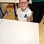 child, boy, glasses, smiling, classroom, desk, chair, school, white_shirt, short_hair, education, happy, indoor, people, furniture, floor, background, person, table, young