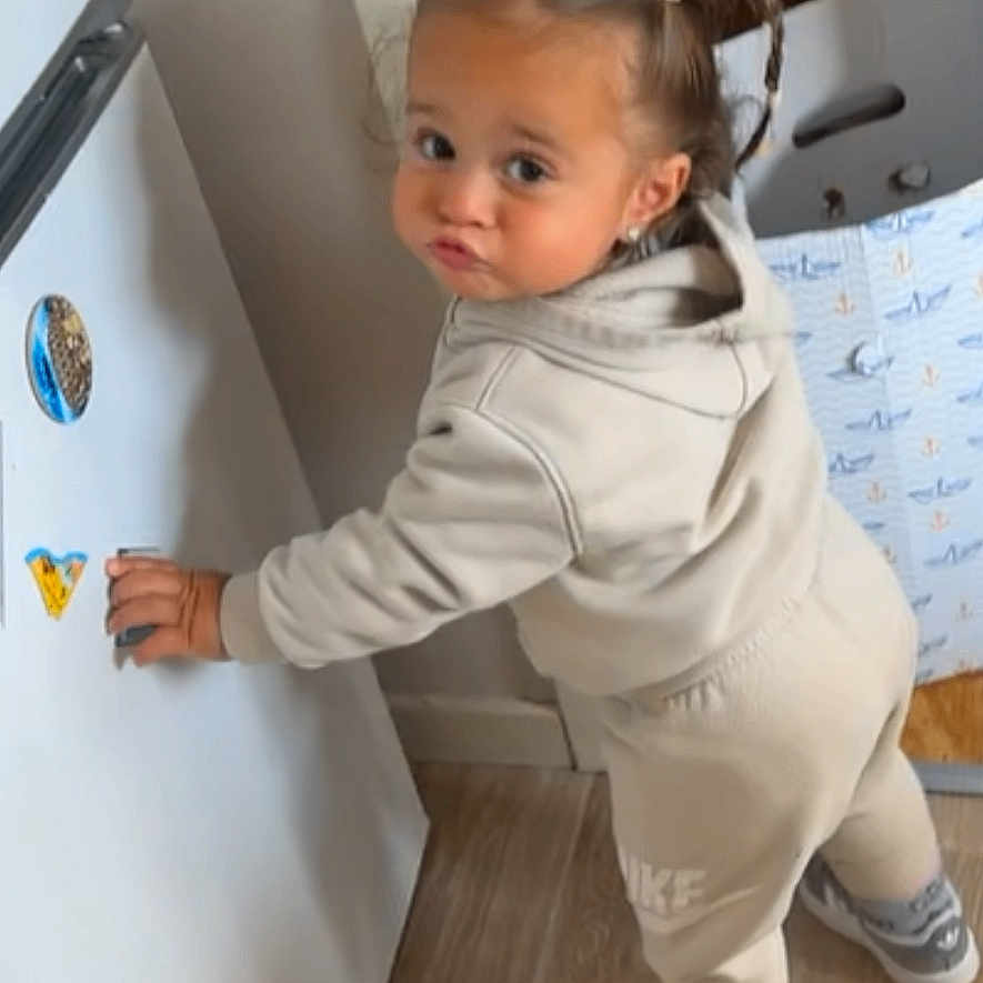Chayna a rejoint le concours — aidez-le/la à gagner de superbes lots ! activity, child, clothing, cute, expression, flooring, fridge, home, hoodie, indoor, magnets, person, pigtails, playful, sneakers, standing, sweatpants, toddler, wooden_floor, young_child