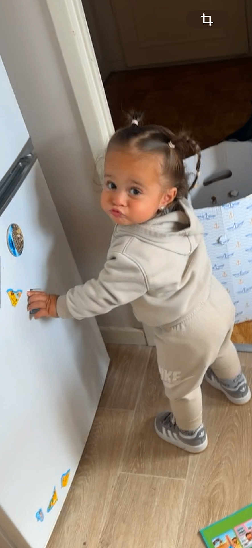 Chayna a rejoint le concours — aidez-le/la à gagner de superbes lots ! toddler, child, pigtails, hoodie, sweatpants, sneakers, fridge, magnets, wooden_floor, indoor, playful, cute, standing, clothing, expression, person, young_child, home, flooring, activity