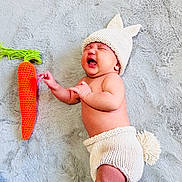 Luna Rose is registered to the contest to win money with this photo: baby, infant, knitted_hat, knitted_diaper, bunny_ears, crocheted_carrot, blanket, soft_texture, cute_expression, lying_down, newborn, baby_clothing, hand, face, skin, toy, plush, indoor, child, cozy