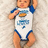 baby, infant, child, portrait, lying_down, smiling, face, detroit_lions, football, sports, onesie, blue_clothing, white_clothing, striped_socks, blanket, fluffy_blanket, indoor, top_down_view, raised_arm, cute
