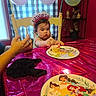 baby, birthday, birthday_party, balloons, cupcake, cake, child, high_chair, eating, frosting, smiling, portrait, indoors, table, tablecloth, plate, disney_princesses, party_hat, adult_hand, celebration