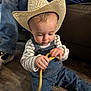 Kamdyn is registered to the contest to win money with this photo: toddler, child, cowboy_hat, denim_overalls, striped_shirt, yellow_rope, floor, indoor, person, playing, seated, hat, footwear, jeans, couch, adult, casual_clothing, hands, headwear, curious