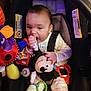 Ezra is registered to the contest to win money with this photo: baby, car_seat, toy, mickey_mouse, plush_toy, infant, child, onesie, colorful, warning_label, seatbelt, indoor, cute, chewing, hand, face, person, sitting, soft_toy, baby_toys