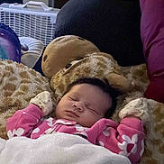 Octavia is registered to the contest to win money with this photo: baby, sleeping, blanket, pink_clothing, mittens, plush_toy, giraffe, couch, cushion, indoor, fan, cozy, child, resting, soft, comfort, person, portrait, home, relaxation