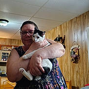 Sydney is registered to the contest to win money with this photo: animal, bench, black_and_white_cat, cat, cozy, curious, dress, furniture, glasses, home_decor, hugging, indoor, light_fixture, person, pet, smile, tattoo, wall_hanging, window, wood_paneling