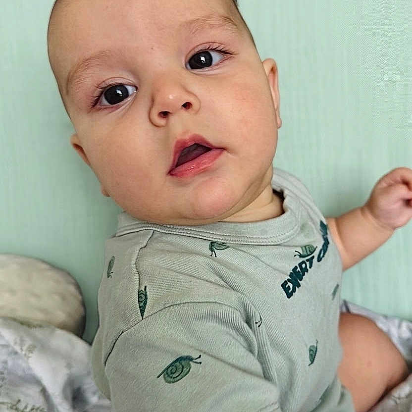 Angel joined the competition — help win amazing prizes! baby, child, infant, face, eyes, mouth, hand, tshirt, snail_print, blanket, soft, curious, sitting, indoors, portrait, skin, head, person, young, cute
