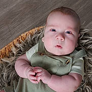 Kyle is registered to the contest to win money with this photo: baby, infant, face, eyes, hands, clothing, romper, basket, fur, texture, wooden_floor, closeup, portrait, cute, child, newborn, skin, expression, indoor, soft_lighting
