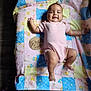 baby, infant, pink_onesie, patchwork_blanket, care_bears, wooden_sign, three_months, smiling, lying_down, child, cute, soft_light, fabric, floor, happy, indoors, person, small_child, blanket, skin