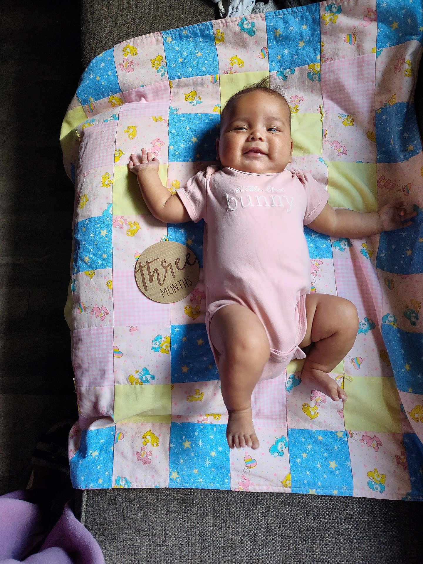 Glorianna joined the competition — help win amazing prizes! baby, infant, pink_onesie, patchwork_blanket, care_bears, wooden_sign, three_months, smiling, lying_down, child, cute, soft_light, fabric, floor, happy, indoors, person, small_child, blanket, skin