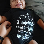 Stephen joined the competition — help win amazing prizes! baby, smiling, onesie, black_clothing, hand, person, face, infant, lying_down, text_on_clothing, glasses_graphic, lightning_bolt, bed, blanket, skin, happy, cute, portrait, child, casual