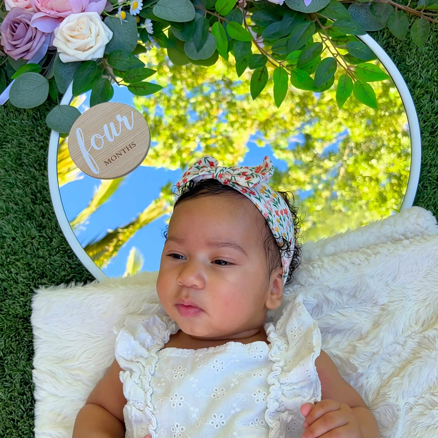 Reign is registered to the contest to win money with this photo: baby, infant, child, portrait, floral_headband, white_dress, smiling, serious_expression, lying_down, blanket, mirror, flowers, roses, greenery, grass, outdoor, garden, nature, reflection, baby_photoshoot