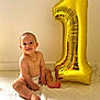 baby, birthday_balloon, blanket, celebration, cute, diaper, first_birthday, floor, gold_balloon, indoor, infant, necklace, number_one, portrait, sitting, smiling, toddler, toes, wall, white_background