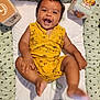 Théo participe au concours pour gagner de l'argent avec cette photo : baby, infant, smiling, yellow_clothing, romper, lying_down, soft_cushion, heart_pattern, toy_blocks, simba, lion_king, playful, happy, child, cute, indoors, skin_tone, kicking_feet, joyful, expression