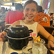 Stella participe au concours pour gagner de l'argent avec cette photo : child, girl, smile, restaurant, food, pot, glass, drink, table, people, indoor, happy, bracelet, white_shirt, dining, meal, crowd, background, portrait, casual