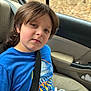 child, car, seatbelt, blue_shirt, shark_graphic, long_hair, young, casual_clothing, window, car_interior, seat, portrait, sitting, indoors, person, face, expression, relaxed, daylight, travel