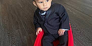 Elias is registered to the contest to win money with this photo: toddler, child, toy_wagon, red, black_suit, indoor, wooden_floor, serious_expression, curly_hair, person, small_wheels, flooring, household, stroller, folding_chair, door, corner, hands, socks, young_child