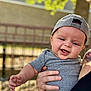 baby, child, smiling, cap, gray_shirt, tattoo, hand, outdoor, fence, sunlight, portrait, happy, person, skin, holding, casual_clothing, infant, daylight, nature, cute