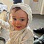 toddler, child, hood, white_jacket, smile, indoor, carpet, shoes, stroller, face, curious, baby, warm_clothing, person, cute, young_child, portrait, cozy, home, expression