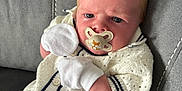 Harland is registered to the contest to win money with this photo: baby, blond_hair, blue_eyes, child, closeup, clothing, couch, cozy, cute, grey_couch, indoors, infant, knit_sweater, pacifier, person, portrait, serious_expression, sitting, soft_fabric, white_mittens