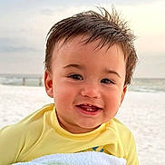 Dj is registered to the contest to win money with this photo: baby, child, beach, seashore, sand, ocean, water, outdoors, portrait, smiling, happy, face, head, yellow_clothing, infant, sunlight, shoreline, sea, cute, photography