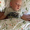 toddler, sleeping, bed, pillow, blanket, floral_pattern, child, face, closed_eyes, shirt, monster_truck, comfort, indoors, rest, peaceful, cute, person, young_child, cozy, nap