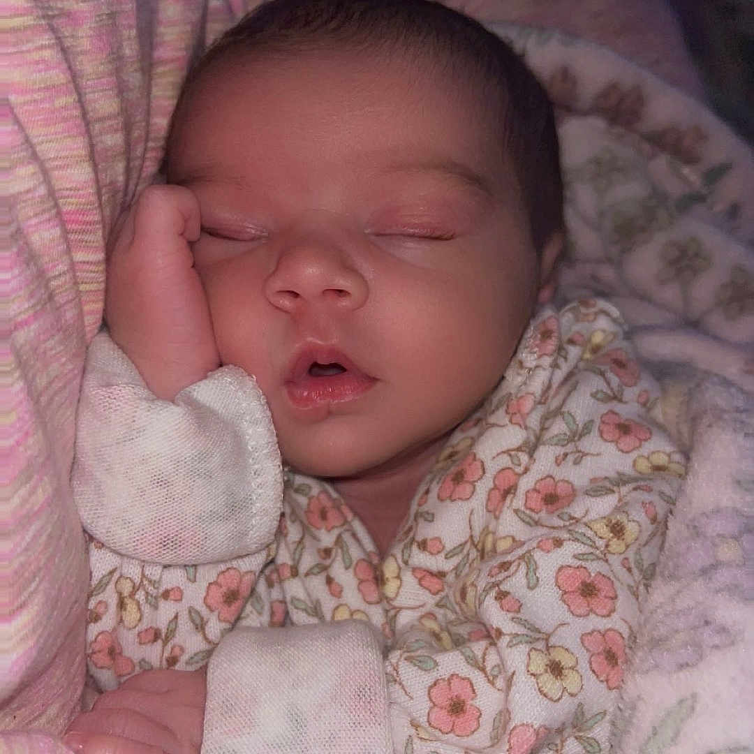 Arabella is registered to the contest to win money with this photo: baby, sleeping, infant, pajamas, blanket, cozy, floral_pattern, hand, face, peaceful, soft_lighting, indoors, closeup, cute, newborn, child, resting, portrait, warm, comfort
