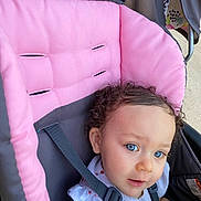 Zella joined the competition — help win amazing prizes! toddler, child, stroller, curly_hair, blue_eyes, pink, gray, seatbelt, outdoor, baby_clothes, infant, cute, person, portrait, sitting, daylight, young_child, face, expression, casual