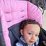 toddler, child, stroller, curly_hair, blue_eyes, pink, gray, seatbelt, outdoor, baby_clothes, infant, cute, person, portrait, sitting, daylight, young_child, face, expression, casual