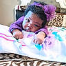 baby, infant, child, portrait, purple_outfit, hair_bow, curly_hair, lying_down, blanket, bed, bedding, zebra_print, bedroom, indoors, face, eyes, hands, looking_at_camera, colorful, adorable