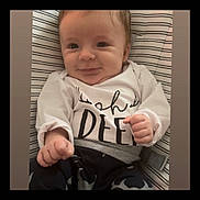Ottus is registered to the contest to win money with this photo: baby, infant, smile, face, clothing, white_shirt, pants, striped_background, cushion, hand, fist, cute, child, person, young, portrait, indoors, happy, sitting, expression