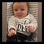 baby, infant, smile, face, clothing, white_shirt, pants, striped_background, cushion, hand, fist, cute, child, person, young, portrait, indoors, happy, sitting, expression