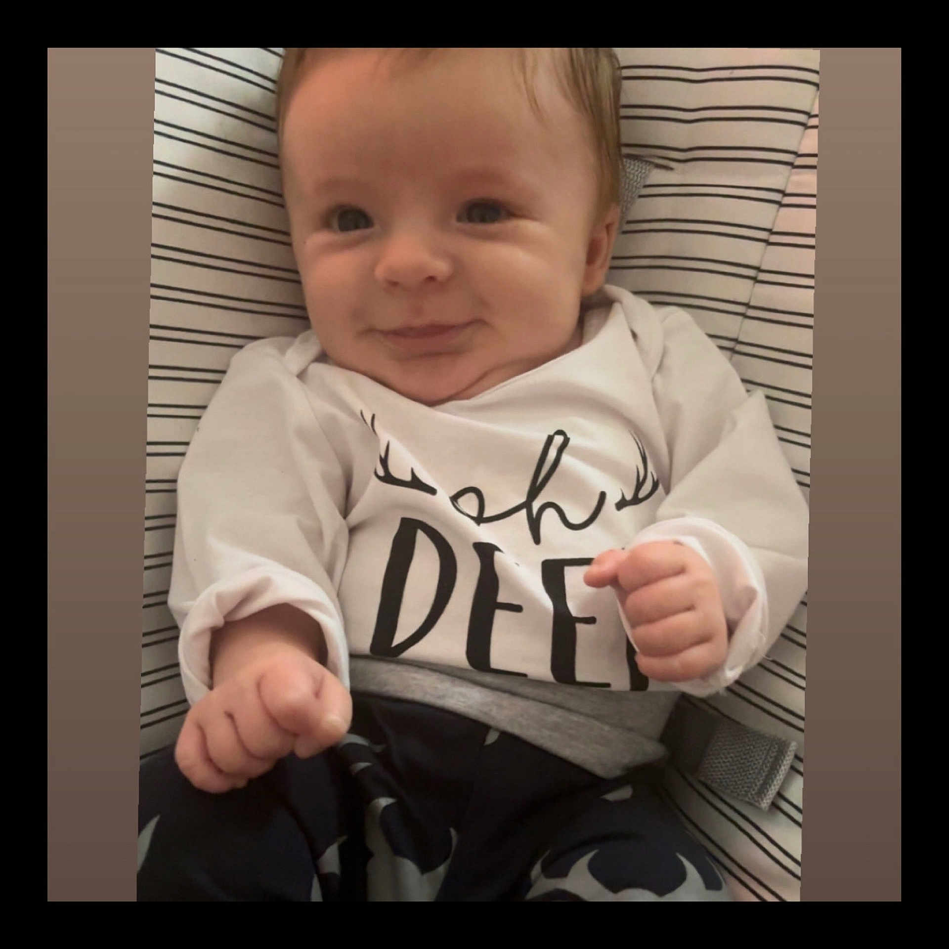 Ottus is registered to the contest to win money with this photo: baby, child, clothing, cushion, cute, expression, face, fist, hand, happy, indoors, infant, pants, person, portrait, sitting, smile, striped_background, white_shirt, young