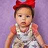 baby, child, red_bow, purple_background, overalls, cartoon_print, curious_expression, wide_eyes, sitting, infant, cute, portrait, clothing, cute_baby, indoor, studio_shot, small_child, headwear, pink_shirt, striped_socks