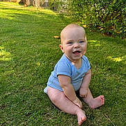 Jude is registered to the contest to win money with this photo: baby, child, grass, outdoor, smiling, blue_clothing, sitting, greenery, nature, sunlight, trees, bushes, happy, cute, infant, skin, barefoot, daylight, young_child, portrait
