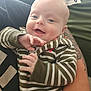 Thomas is registered to the contest to win money with this photo: baby, infant, smiling, striped_clothing, hand, tattoo, arm, person, portrait, happy, indoor, cute, child, skin, face, young, cozy, holding, casual, expression