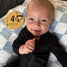 baby, black_onesie, blanket, blue_eyes, checkered_pattern, child, cute, face, hand, happy, indoors, infant, lying_down, milestone, monkey_illustration, portrait, smile, soft_texture, wooden_sign, young