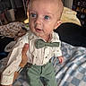 Sy is registered to the contest to win money with this photo: adult_hand, baby, bedroom, blanket, blue_eyes, bow_tie, child, clothing, curious, cute, furniture, green_pants, hand, home, indoor, person, portrait, shirt, soft_lighting, suspenders