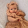 baby, infant, crochet, headband, flower, blanket, knitted, soft_texture, cute, portrait, child, clothing, hand, face, young, lying_down, cozy, warm_colors, expression, indoors