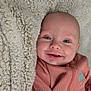 baby, smile, blanket, pink_clothing, nike_logo, drool, face, blue_eyes, infant, cozy, soft_texture, lying_down, cute, indoor, person, happy, child, head, apparel, closeup