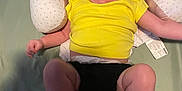 Rosalie joined the competition — help win amazing prizes! baby, child, smiling, yellow_shirt, black_diaper_cover, pillow, cushion, lying_down, happy, infant, person, indoor, bed, fabric, skin, head, arms, legs, face, expression