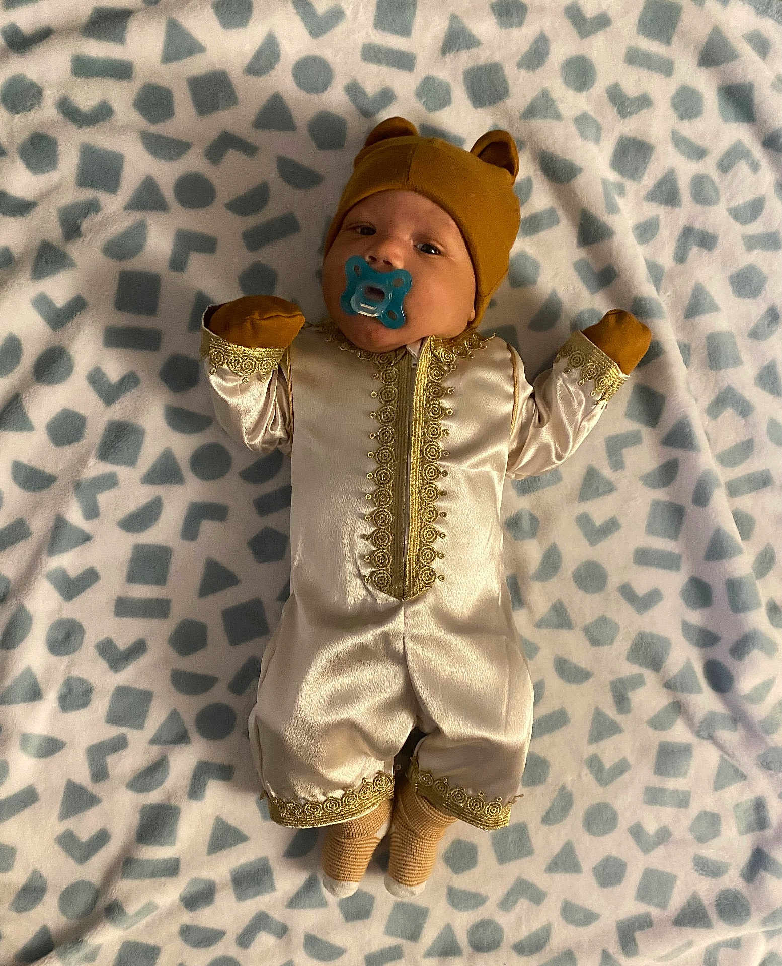 Aahil is registered to the contest to win money with this photo: baby, pacifier, hat, bear_ears, blanket, pattern, gold_embroidery, clothing, infant, cute, lying_down, sock, soft, fabric, portrait, child, indoors, resting, adorable, young