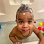 toddler, child, bathtub, foam, shampoo, water, colorful_balls, bath_time, smiling, face, hands, necklace, wet_skin, indoor, playful, cute, portrait, young_child, happy, looking_up