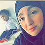 woman, child, toddler, indoor, selfie, hijab, smile, couch, white_couch, tufted_couch, curly_hair, casual_clothing, portrait, seated, home_interior, red_shoes, white_shirt, black_hijab, thoughtful, family