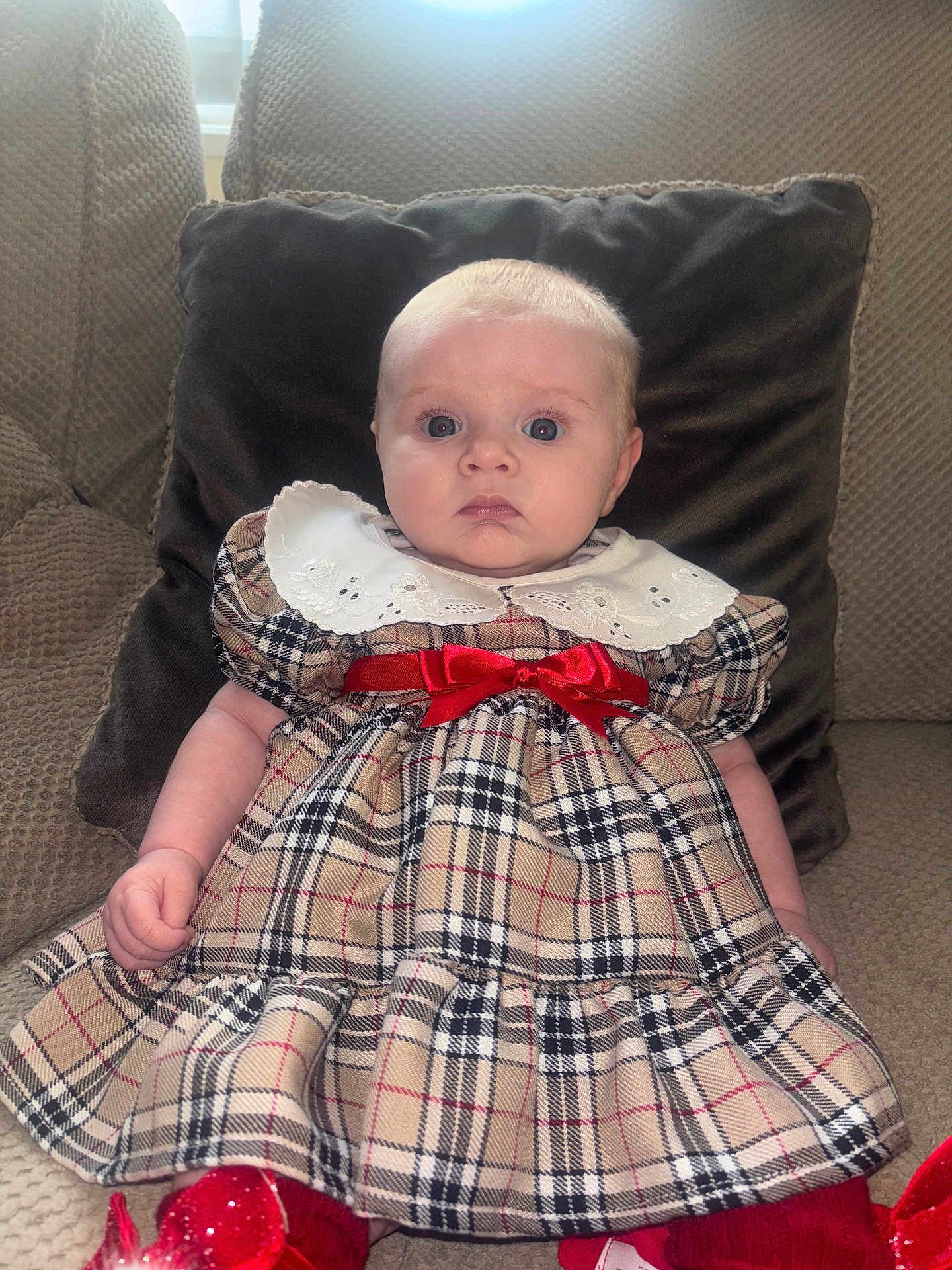 Ariella-Rae joined the competition — help win amazing prizes! baby, child, plaid_dress, red_bow, couch, pillow, indoor, portrait, cute, young_child, sitting, expression, face, person, clothing, furniture, window, light, home, sock