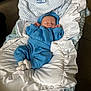 baby, bed, blanket, blue_clothing, carrying_bassinet, cozy, cute, head, indoors, infant, nap, newborn, peaceful, person, resting, ruffled_blanket, sleeping, sock, soft_fabric, white_blanket