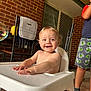 Silas joined the competition — help win amazing prizes! baby, high_chair, smile, child, indoor, brick_wall, chair, cushion, person, footwear, shorts, sneakers, happy, table, hands, blond_hair, face, young_child, casual_clothing, home