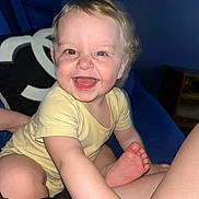 Silas is registered to the contest to win money with this photo: baby, child, smile, laugh, yellow_onesie, hands, feet, face, blue_background, cushion, indoor, cute, happy, person, infant, portrait, skin, expression, seated, closeup