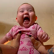 Emma is registered to the contest to win money with this photo: adorable, baby, barbie, ceiling, close_up, excited, hands, holding, indoor, infant, joyful, laughing, mouth_open, onesie, person, pink_clothing, portrait, smiling, tattooed_hands, tongue