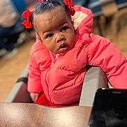 Teja joined the competition — help win amazing prizes! toddler, child, puffer_jacket, red_bows, curious, indoor, table, phone, portrait, person, young_child, seated, winter_clothing, cute, face, expression, hair, closeup, fashion, candid
